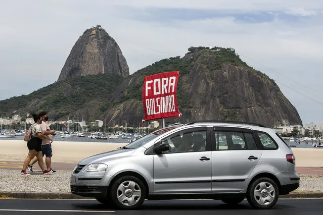 People hold a sign that reads “Bolsonaro out”, during a protest against the government's response in combating COVID-19 and demanding the impeachment of Brazilian President Jair Bolsonaro, backdropped by the Sugar Loaf mountain in Rio de Janeiro, Brazil, Sunday, January 31, 2021. (Photo by Bruna Prado/AP Photo)