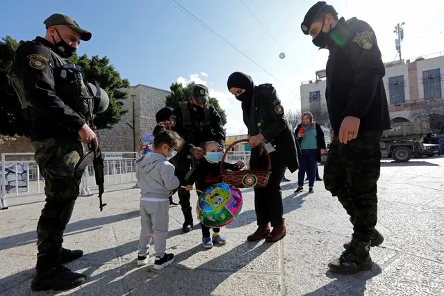 A member of Palestinian security forces distributes sweets to children at Manger Square ahead of Christmas in Bethlehem in the Israeli-occupied West Bank on December 23, 2020. (Photo by Mussa Qawasma/Reuters)