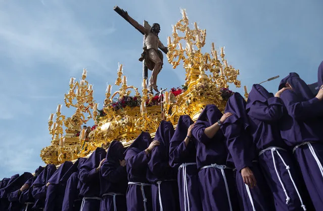 Penitents of “Salud” brotherhood are seen carrying an ornate float with the statue of Christ as they take part in a procession during the Palm Sunday, to mark the Holy Week celebrations in Malaga, Spain on April 10, 2022. After two years without Holy Week due to the coronavirus pandemic, thousands of faithful wait to see the processions bearing the statues of Christ and the Virgin Mary on the streets as part of traditional Holy Week. In Andalusia, the Holy Week celebration congregates thousands of people from all countries, and it's considered one of the most important religious and cultural events of the year. (Photo by Jesus Merida/SOPA Images/LightRocket via Getty Images)
