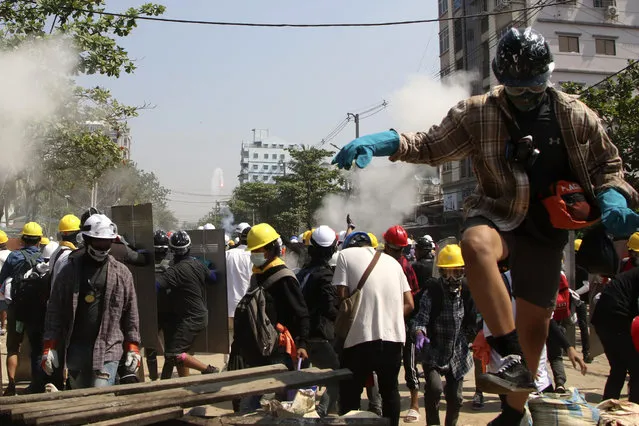 Protesters are dispersed as riot police fired tear gas behind a makeshift barricade in Yangon, Myanmar, Sunday, March 7, 2021. (Photo by AP Photo/Stringer)