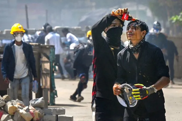 A protester pours Coca-Cola on the face of a comrade to diminish the effects of tear gas during a crackdown by security forces on a demonstration against the military coup in Yangon's Thaketa township on March 19, 2021. (Photo by AFP Photo/Stringer)