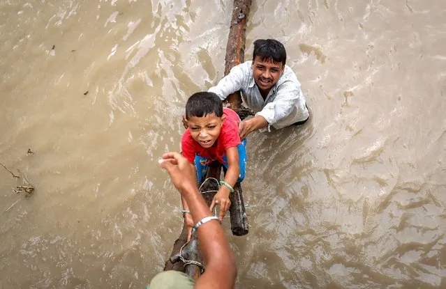 A man helps his son to climb onto a flyover under construction, after being displaced by the rising water level of river Yamuna after heavy monsoon rains in New Delhi, India on July 12, 2023. (Photo by Adnan Abidi/Reuters)