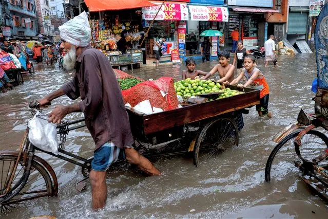 Children push a vegetable seller's cart as streets are flooded amid heavy rains in Dhaka, Bangladesh on June 12, 2023. (Photo by Mohammad Ponir Hossain/Reuters)