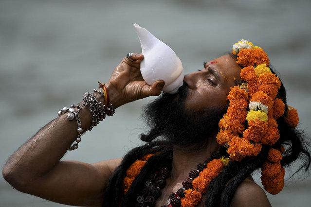 A Naga Sadhu (Hindu holy man) blows a conch as he takes a holy dip in the waters of the Ganges River on the day of Shahi Snan (royal bath) during the ongoing religious Kumbh Mela festival, in Haridwar on April 12, 2021. (Photo by Money Sharma/AFP Photo)