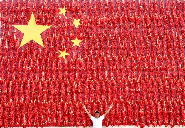A man poses for pictures in front of a giant Chinese flag decorated with red chili peppers on the side of a building, ahead of the Chinese National Day at a village in Mengjin county, Henan province, China September 21, 2018. (Photo by Reuters/China Stringer Network)