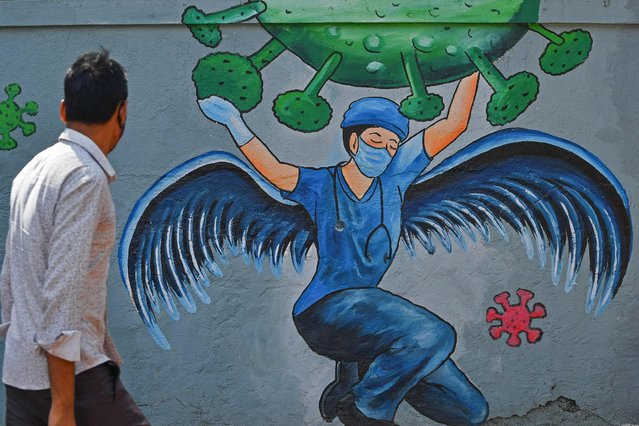 A pedestrian walks past a wall mural representing awareness measures against the Covid-19 coronavirus featuring a frontline medical staff as a guardian angel, in Navi Mumbai on June 7, 2021. (Photo by Indranil Mukherjee/AFP Photo)