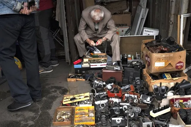 A vendor selling old cameras and accessories sits in his booth at a flea market in Kyiv, Ukraine, Saturday, July 8, 2023. The Pochaina neighborhood in the Ukrainian capital comes alive every weekend as hundreds of people flock to its famous flea market, looking for finds. Antique-hunters, collectors and many others look over seemingly endless rows of trinkets and time-worn wares. (Photo by Jae C. Hong/AP Photo)