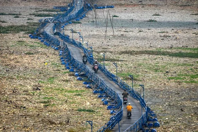 People pass on a floating bridge that some 300m across the dried up Citarum River in Cihampelas, West Java on October 4, 2023. (Photo by Timur Matahari/AFP Photo)