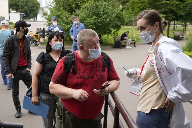 A man speaks to a medical worker as pother people wearing face masks to protect against coronavirus stand in line to get a coronavirus vaccine at a vaccination point in Gorky Park in Moscow, Russia, Wednesday, June 30, 2021. Russia was among the first in the world to announce and deploy a coronavirus vaccine last year, but so far only about 23 million, just over 15% of the population have received at least one vaccine shot. Hampered by widespread vaccine hesitancy and limited production capacity, Russia's vaccination rates have picked up in recent weeks, after authorities in many regions made shots mandatory for employees in certain sectors. (Photo by Alexander Zemlianichenko/AP Photo)