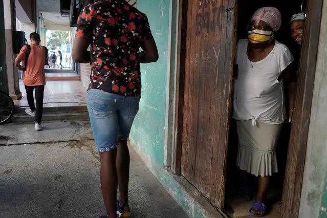 People peer from a door as demonstrators pass by during a protest against and in support of the government, amidst the coronavirus disease (COVID-19) outbreak, in Havana, Cuba on July 11, 2021. (Photo by Alexandre Meneghini/Reuters)