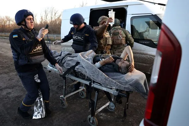 Policemen hand over a man wounded to employees of Ukrainian Emergency Service on a road outside in Avdiivka, Donetsk region, on November 13, 2023, amid the Russian invasion in Ukraine. (Photo by Anatolii Stepanov/AFP Photo)