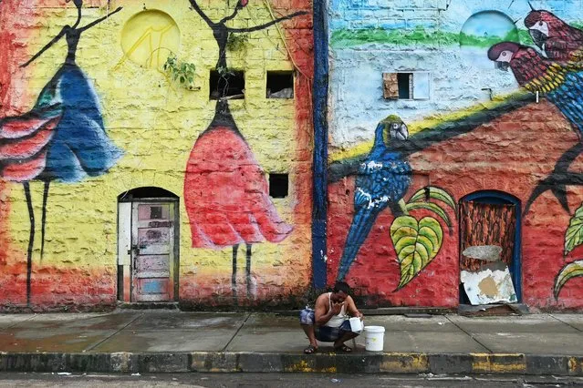 A man washes himself early in the morning outside a warehouse decorated with a wall mural in Mumbai on September 30, 2023. (Photo by Indranil Mukherjee/AFP Photo)