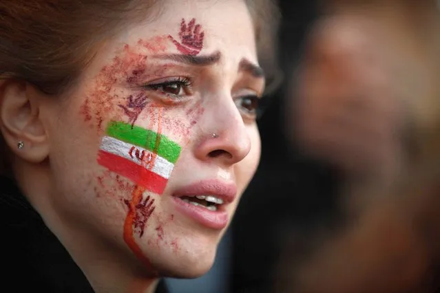 A demonstrator with an Iranian flag and red hands painted on her face attends a rally in support of Iranian protests, in Paris on October 9, 2022, following the death of Iranian woman Mahsa Amini in Iran. NGO Iran Human Rights (IHR) has counted 95 deaths in the repression of protests following the death of Amini, 22, who died in custody on September 16, 2022, three days after her arrest by the police in Tehran for allegedly breaching the Islamic republic's strict dress code for women. (Photo by Julien de Rosa/AFP Photo)