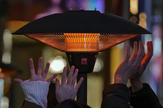 People try to keep warm their hands by a heater as they wait for their seats outside a restaurant at an outdoor shopping mall in Beijing, Saturday, December 23, 2023. A cold wave began earlier in the week bringing extensive snowfall and freezing temperatures across China. (Photo by Andy Wong/AP Photo)