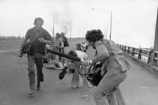 Unidentified members of a television news crew run for cover in Saigon on Monday, April 28, 1975 during fighting between South Vietnamese Government troops and Communist forces on the northern outskirts of Saigon. (Photo by Thauh Nuy/AP Photo)