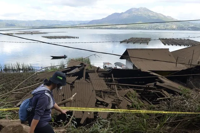 A woman walks past houses by Lake Batur which were damaged by an earthquake-triggered landslide in Bangli, on the island of Bali, Indonesia, Saturday, October 16, 2021. A few people were killed and another several were injured when a moderately strong earthquake and an aftershock hit the island early Saturday. (Photo by Dewa Raka/AP Photo)