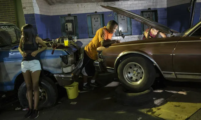 Men spend the evening repairing a car outside their home as a young woman pops chewing gum in Caracas, Venezuela, Friday, May 10, 2019. (Photo by Rodrigo Abd/AP Photo)
