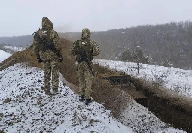 In this image provided by the Ukrainian Board Guard Press Office, Ukrainian border guards watch as a special vehicle digs a trench on the Ukraine-Russia border close to Sumy, Ukraine, Tuesday, December 21, 2021. (Photo by Ukrainian Board Guard Press Office via AP Photo)
