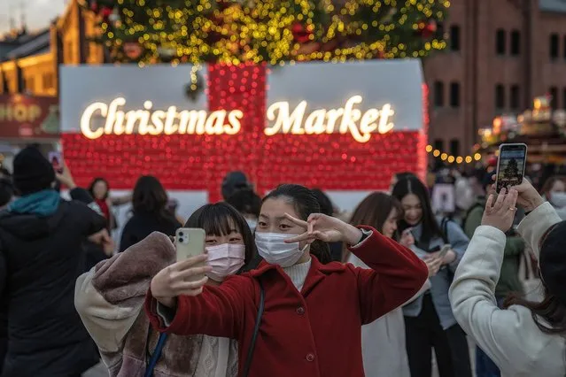 Women wearing face masks take a selfie photograph as they visit a Christmas market on December 23, 2021 in Yokohama, Japan. The Japanese government has stated they will not immediately retighten restrictions after the first case of community transmission of the Omicron coronavirus variant was confirmed in Osaka yesterday. (Photo by Carl Court/Getty Images)