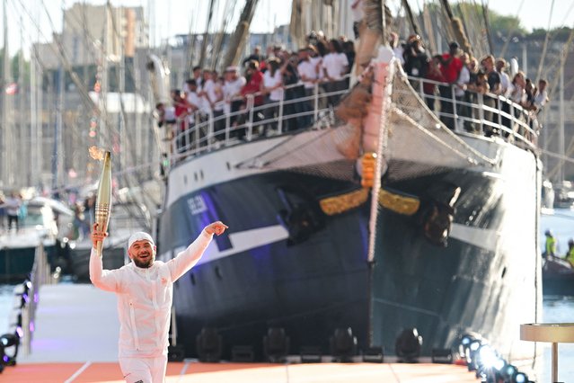 French rapper Julien Mari aka Jul gestures and holds the Olympic Torch during the Olympic Flame arrival ceremony at the Vieux-Port (Old Port), ahead of the Paris 2024 Olympic and Paralympic Games, in Marseille, southeastern France, on May 8, 2024. The transfer of the flame onshore from a 19th-century tall ship will mark the start of a 12,000-kilometre (7,500-mile) torch relay across mainland France and the country's far-flung overseas territories. (Photo by Nicolas Tucat/AFP Photo)