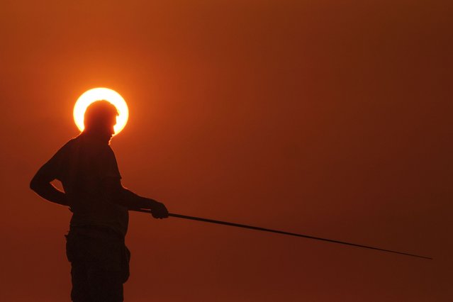 A fisherman is silhouetted against a setting sun as he fishes from a rocky area along the Beirut coastline, in Lebanon, April 15, 2024. (Photo by Hassan Ammar/AP Photo)