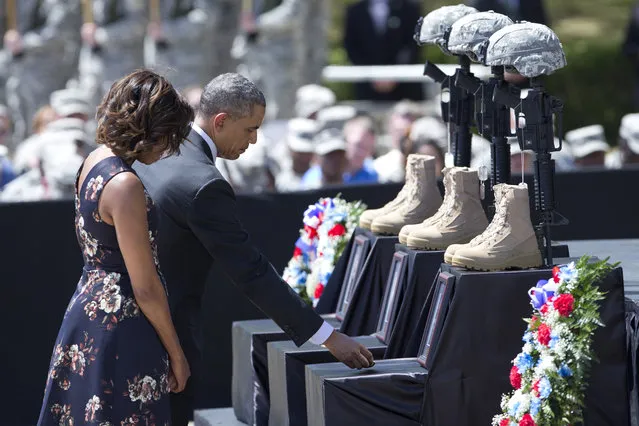 President Barack Obama, accompanied by first lady Michelle Obama, places challenge coins as they pay their respect during a memorial ceremony, Wednesday, April 9, 2014, at Fort Hood Texas, for those killed there in a shooting last week. President Barack Obama is reprising his role as chief comforter as he returns once again to a grief-stricken corner of America to mourn with the families of those killed last week at Fort Hood and offer solace to the nation. (Photo by Carolyn Kaster/AP Photo)