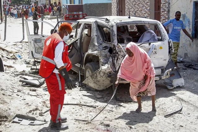 A woman, right, points a medical worker to remains of the suicide bomber at the scene, after Somalia's government spokesperson Mohamed Ibrahim Moalimuu was wounded in a suicide bombing in Mogadishu, Somalia, Sunday, January 16, 2022. Moalimuu appeared to be the sole target of the attack near his residence by a busy intersection in the capital, for which the al-Shabab extremist group has claimed responsibility. (Photo by Farah Abdi Warsameh/AP Photo)