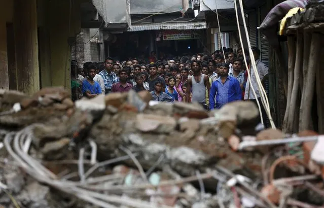 Onlookers stand at the site of a collapsed building in New Delhi, India, July 19, 2015. (Photo by Adnan Abidi/Reuters)