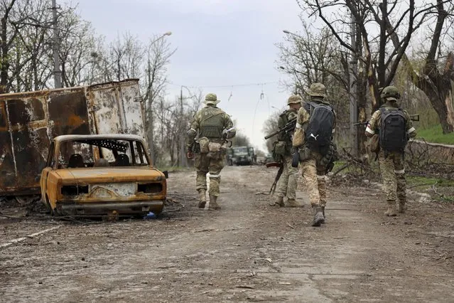Servicemen of Donetsk People's Republic militia walk past damaged vehicles during a heavy fighting in an area controlled by Russian-backed separatist forces in Mariupol, Ukraine, Tuesday, April 19, 2022. Taking Mariupol would deprive Ukraine of a vital port and complete a land bridge between Russia and the Crimean Peninsula, seized from Ukraine from 2014. (Photo by Alexei Alexandrov/AP Photo)
