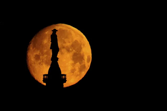 The moon sets behind a statue of William Penn atop of City Hall in Philadelphia, Wednesday, March 16, 2022. (Photo by Matt Rourke/AP Photo)