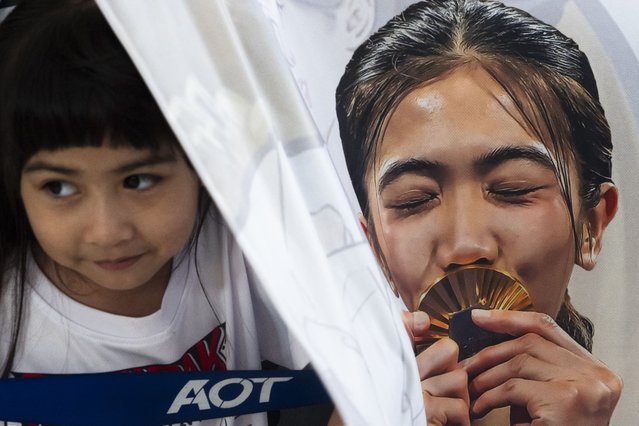 A child (L) stands behind a banner of Thailand's taekwondo gold medallist Panipak Wongpattanakit while waiting to greet athletes on their return to Thailand from the Paris 2024 Olympic Games, at Suvarnabhumi International Airport in Bangkok on August 13, 2024. (Photo by Chanakarn Laosarakham/AFP Photo)