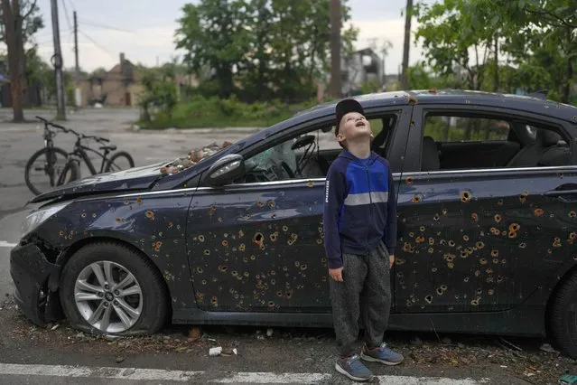 A child standing next to a damaged car looks up at a building destroyed during attacks in Irpin, on the outskirts Kyiv, Ukraine, Monday, May 30, 2022. (Photo by Natacha Pisarenko/AP Photo)