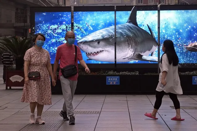 Residents wearing masks walk past a display showing a shark, Wednesday, June 1, 2022, in Shanghai. (Photo by Ng Han Guan/AP Photo)