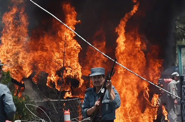 An Afghan policeman stands guard as smoke and flames rise from the site of a huge blast struck near the entrance of Kabul's international airport, in Kabul on August 10, 2015. A huge blast struck near the entrance of Kabul's international airport on August 10 during the peak lunchtime period, officials said, warning that heavy casualties were expected. (Photo by Shah Marai/AFP Photo)