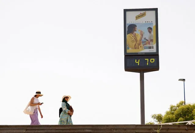 Women walk next to a thermometer displaying 47 Celsius degrees (116.6 Fahrenheit degrees) during the first heatwave of the year in Seville, Spain on June 11, 2022. (Photo by Marcelo del Pozo/Reuters)