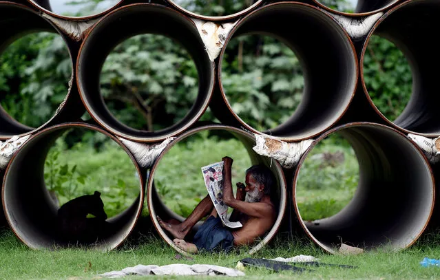 An Indian man reads a newspaper as he sits inside a pipe in New Delhi on August 2, 2017. (Photo by Money Sharma/AFP Photo)