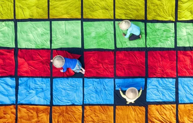 Hundreds of squares of colourful fabric are laid out to dry by workers in Bogor, Indonesia on June 9, 2022. Having been dyed, the material is left outside in the 30-degree heat on a field, before they are used to make tablecloths. (Photo by Gatot Herliyanto/Solent News)