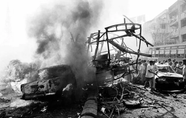 The skeletal remains of a transport bus are seen alongside burning vehicles and damaged buildings outside Bombay's Passport Office after a massive explosion, March 12, 1993. Twelve bombs exploded in less than 20 minutes at various locations, killing hundreds in India's financial capital. According to the Bombay Police, the prime culprit Dawood Ibrahim, who masterminded the attacks, is still at large and lives as a “free man” in Karachi, Pakistan. (Photo by Sherwin Crasto/AP Photo/File)