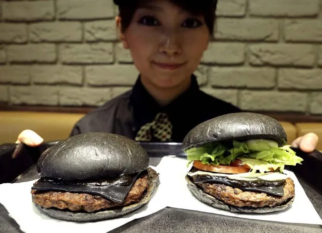 Burger King employee Rumi Sekine shows the Kuro Diamond burger, right, and the Kuro Pearl burger at its Shibuya restaurant in Tokyo Tuesday, September 16, 2014. The international hamburger chain in Japan will launch the two new “kuro burger”, or “black burger” menus that sport buns, cheese and sauce all in black color, starting on Friday, Sept. 19, for a limited period. The buns and cheese are darkened with bamboo charcoal while the beef patties made with black-pepper are topped with the garlic sauce using squid ink. (Photo by Koji Sasahara/AP Photo)