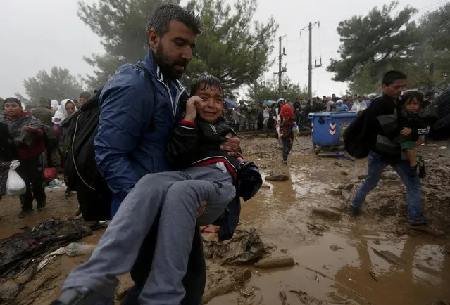 A Syrian refugee carries his child through the mud as they cross the border from Greece into Macedonia during a rainstorm, near the Greek village of Idomeni, September 10, 2015. (Photo by Yannis Behrakis/Reuters)