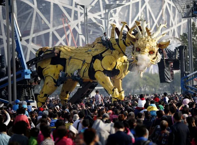 People watch a mechanical installation named “Long Ma” emit water vapour during the Long Ma performance in front of the National Stadium, also known as the Bird's Nest, in Beijing October 17, 2014. “Long Ma”, a 17-meter (56-ft) long and 15-meter (49-ft) tall mechanized dragon sculpture, and “The Spider”, a 5.7-meter (19-ft) tall and 6-meter (20-ft) wide machine, are operated by French performance art company La Machine. (Photo by Kim Kyung-Hoon/Reuters)