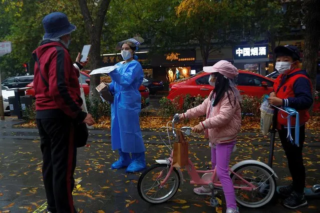 A worker in a protective suit guides people to scan health QR code at a nucleic acid test booth for the coronavirus disease (COVID-19), in Beijing, China on November 15, 2022. (Photo by Tingshu Wang/Reuters)