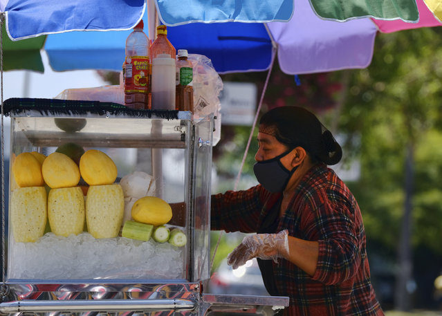 A masked fruit vendor prepares her streetside cart while waiting for customers near downtown Los Angeles on Wednesday, August 5, 2020. California lawmakers are considering requiring employers to notify workers and public health officials about positive COVID-19 cases in the workplace. Violators could be charged with a misdemeanor and assessed a fine of up to $10,000. Supporters say the bill is necessary to protect workers. But business groups say the bill is so vague it will be impossible to comply with. (Photo by Richard Vogel/AP Photo)