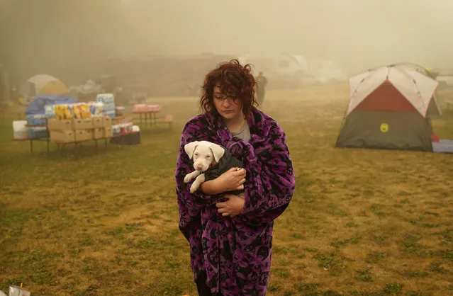 Shayanne Summers holds her dog Toph while wrapped in a blanket after several days of staying in a tent at an evacuation center at the Milwaukie-Portland Elks Lodge, Sunday, September 13, 2020, in Oak Grove, Ore. “It's nice enough here you could almost think of this as camping and forget everything else, almost”, said Summers about staying at the center after evacuating from near Molalla, Oregon which was threatened by the Riverside Fire. (Photo by John Locher/AP Photo)