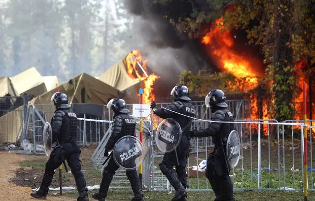 Slovenian policemen walk as a fire sweeps through a migrant camp in Brezice, Slovenia, October 21, 2015. The cause of the fire was not immediately known but many of the camp's tents were destroyed in the blaze. (Photo by Zeljko Lukunic/Reuters/Pixell)