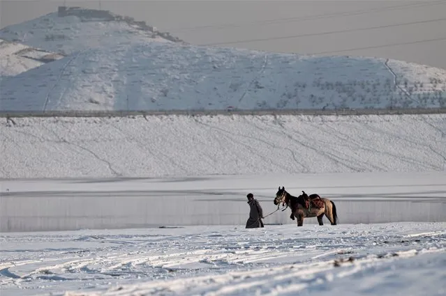 An Afghan youth with his horse walks along the Qargha Lake on the outskirts of Kabul on January 26, 2023. (Photo by Wakil Kohsar/AFP Photo)