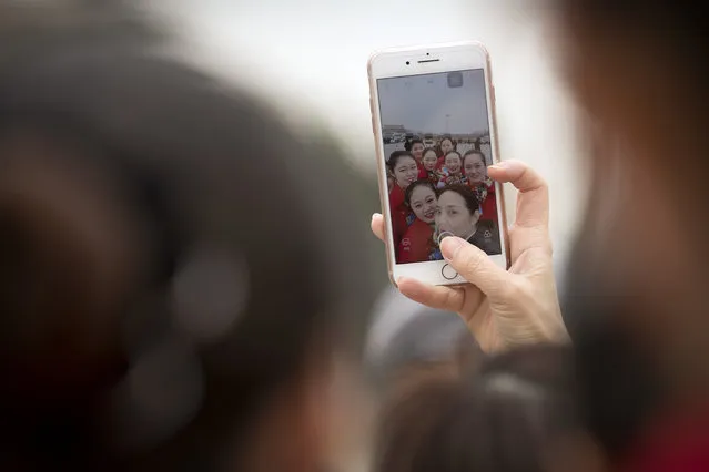 Hospitality staffers are reflected in a cellphone screen as they pose for a selfie during a meeting at the Great Hall of the People ahead of Monday's opening session of China's National People's Congress (NPC) in Beijing, Sunday, March 4, 2018. (Photo by Mark Schiefelbein/AP Photo)