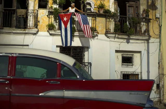 In this  July 20, 2015, file photo, Javier Yanez looks out from his balcony where he hung a U.S., and a Cuban national flag, to celebrate the restored full diplomatic relations between Cuba and the Unites States, in Old Havana. The Cuban government has not announced any big deals with American companies since December 17. (Photo by Ramon Espinosa/AP Photo)