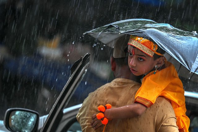 A man carries his son dressed as the Hindu god Krishna ahead of Janmashtami celebrations during rainfall in New Delhi on August 14, 2025. (Photo by Arun Sankar/AFP Photo)