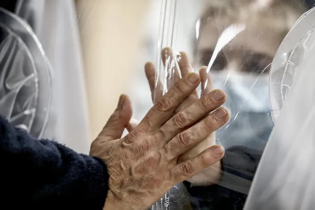 Relatives touch each other's hand through a plastic film screen and a glass to avoid contracting COVID-19 at the San Raffaele center in Rome, Tuesday, December 22, 2020. Italians are easing into a holiday season full of restrictions, and already are barred from traveling to other regions except for valid reasons like work or health. Starting Christmas eve, travel beyond city or town borders also will be blocked, with some allowance for very limited personal visits in the same region. (Photo by Cecilia Fabiano/LaPresse via AP Photo)